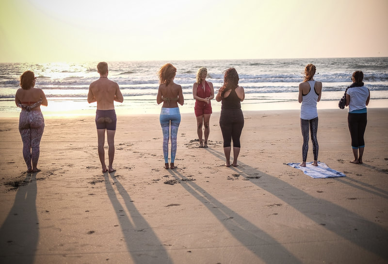 Yoga students standing in meditation on a beach in Goa at sunset